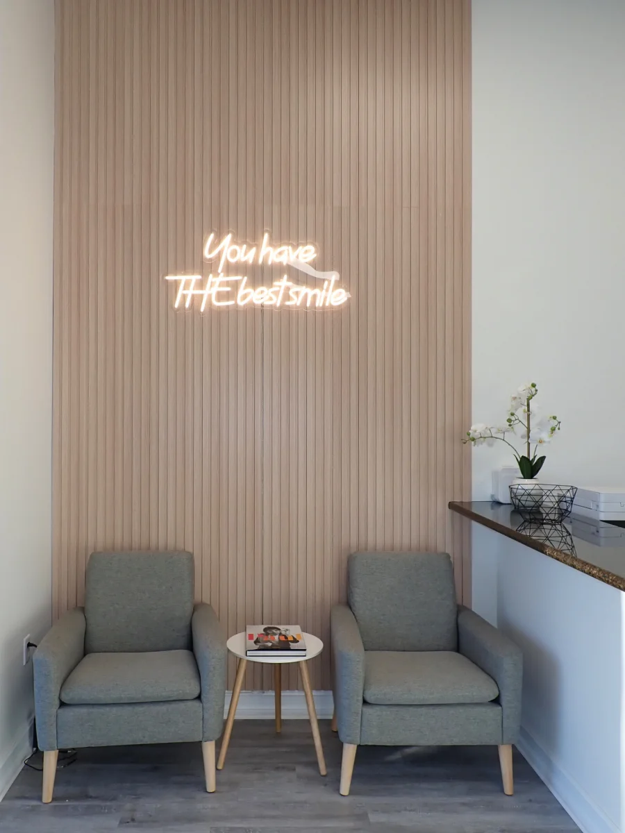 Cozy waiting nook with a 'You have THE best smile' neon sign in the Miami Lakes office